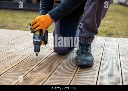 Costruzione di ponti o terrazze, costruttore manuale con cacciavite elettrico che installa tavole di legno impregnate Foto Stock