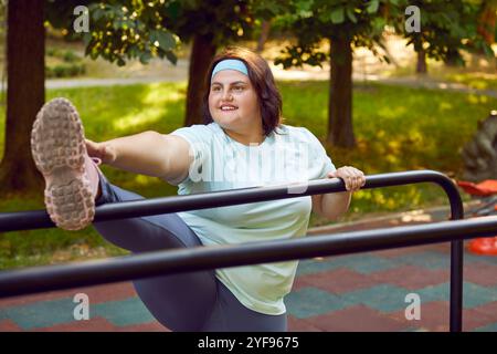 Giovane donna felice in sovrappeso che fa esercizio di stretching sul campo sportivo del parco cittadino Foto Stock