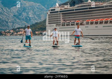 tre pagaiatori in un'avventura panoramica di fronte a una maestosa nave da crociera con sfondo di montagna Foto Stock
