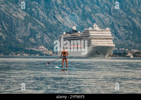 pagaia da solo di fronte a una torreggiante nave da crociera con uno splendido sfondo montuoso Foto Stock