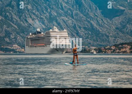 pagaia da solo di fronte a una torreggiante nave da crociera con uno splendido sfondo montuoso Foto Stock