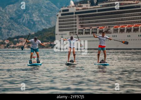tre pagaiatori in un'avventura panoramica di fronte a una maestosa nave da crociera con sfondo di montagna Foto Stock