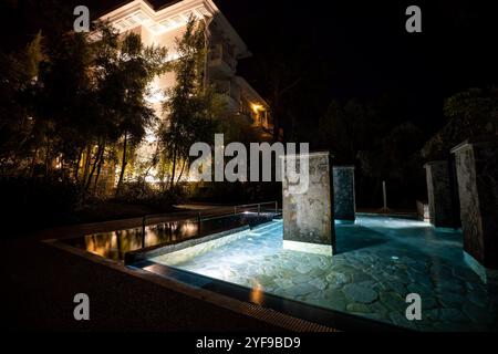 Rilassatevi in un lussuoso resort turistico con una piscina splendidamente illuminata, creando un ambiente tranquillo sotto le stelle di notte Foto Stock