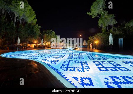 Rilassatevi in un lussuoso resort turistico con una piscina splendidamente illuminata, creando un ambiente tranquillo sotto le stelle di notte Foto Stock