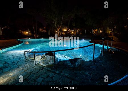 Rilassatevi in un lussuoso resort turistico con una piscina splendidamente illuminata, creando un ambiente tranquillo sotto le stelle di notte Foto Stock