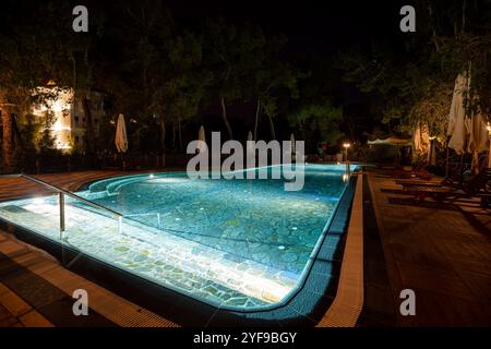 Rilassatevi in un lussuoso resort turistico con una piscina splendidamente illuminata, creando un ambiente tranquillo sotto le stelle di notte Foto Stock