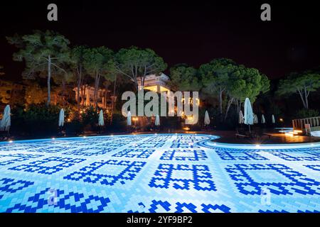 Rilassatevi in un lussuoso resort turistico con una piscina splendidamente illuminata, creando un ambiente tranquillo sotto le stelle di notte Foto Stock