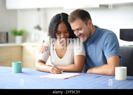 Felice coppia affettuosa che firma un contratto di carta nella cucina di casa Foto Stock