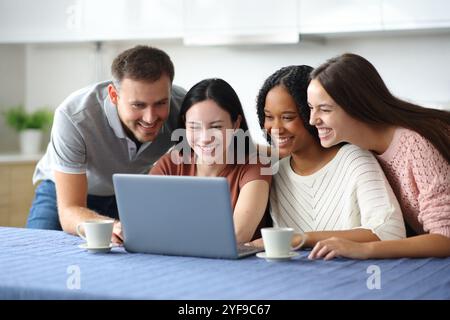Quattro amici interrazziali felici che controllano i contenuti multimediali online del portatile in cucina a casa Foto Stock