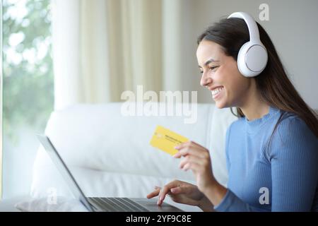 Donna felice che indossa le cuffie che acquista contenuti multimediali tramite laptop e carta di credito online Foto Stock