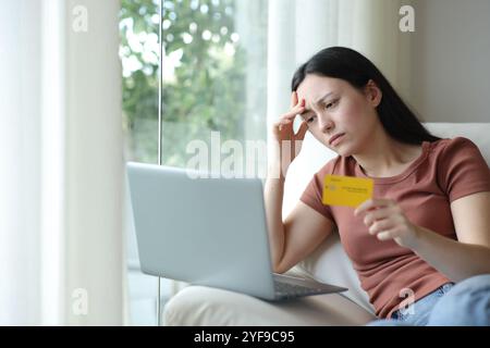 Preoccupata donna asiatica che si lamenta di avere problemi ad acquistare online con carta di credito e laptop a casa Foto Stock
