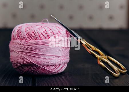 Forbici vintage dorate e uno spiedino rosa pallido di filo di seta per la lavorazione degli aghi giacciono su un tavolo di legno scuro. Minimalismo nella foto. Foto Stock