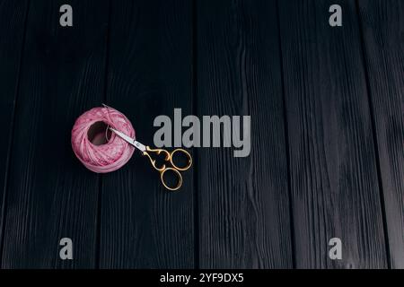 Forbici vintage dorate e uno spiedino rosa pallido di filo di seta per la lavorazione degli aghi giacciono su un tavolo di legno scuro. Minimalismo nella foto. Foto Stock