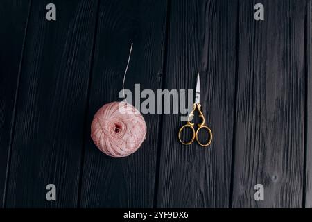 Forbici vintage dorate e uno spiedino rosa pallido di filo di seta per la lavorazione degli aghi giacciono su un tavolo di legno scuro. Minimalismo nella foto. Foto Stock