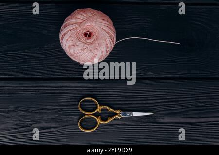 Forbici vintage dorate e uno spiedino rosa pallido di filo di seta per la lavorazione degli aghi giacciono su un tavolo di legno scuro. Minimalismo nella foto. Foto Stock