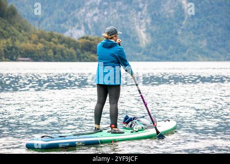 Vista posteriore della donna in Sportswear canottaggio con tavola SUP su Calm Water, godendosi Serenity e fitness Foto Stock