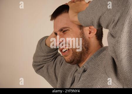 Uomo in depressione. Ritratto di un ragazzo che chiude le orecchie per mano e tiene gli occhi chiusi mentre è isolato sul grigio. Foto di disperato infastidito Foto Stock