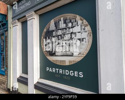 Vetrina per pernici, un'azienda di decorazione per la casa, High Street, Hadleigh, Suffolk, Regno Unito; presenta una vecchia foto degli interni con due addetti al banco Foto Stock