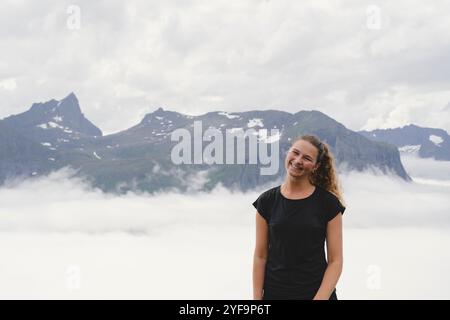 Allegra giovane donna in piedi con nuvole contro le montagne Foto Stock