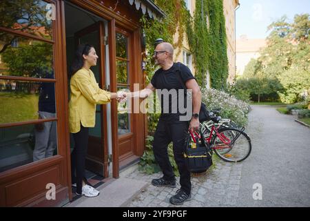 Donna matura felice che saluta il riparatore mentre si trova alla porta dell'edificio residenziale Foto Stock