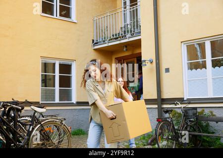 Bella giovane donna che porta una scatola di cartone contro l'edificio Foto Stock