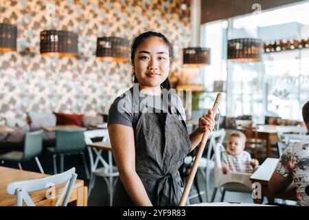 Ritratto di una giovane cameriera che tiene in mano il mocio mentre è in piedi in un bar Foto Stock