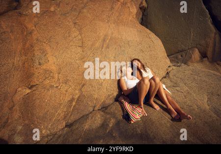 Amiche sorridenti che si guardano mentre si siedono sulla roccia Foto Stock