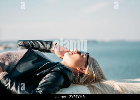 Una giovane donna gode di un momento di relax all'aperto vicino all'acqua scintillante, deliziandosi con la calda luce del sole Foto Stock