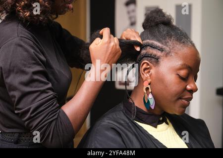 Parrucchiere che fa trecce all'uncinetto a un cliente in un parrucchiere Foto Stock