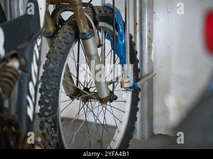 La vecchia ruota anteriore della vecchia bicicletta ruggine è bloccata e fissata al portabiciclette in metallo con catena e lucchetto. Foto Stock