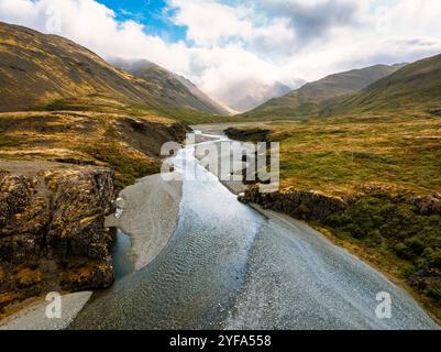 Splendida vista aerea di un fiume islandese che si snoda attraverso una valle circondata da aspre colline e montagne nebbiose, catturando la bellezza selvaggia e seren Foto Stock