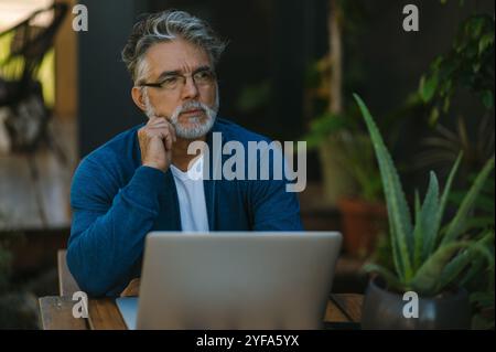 Un bell'uomo di mezza età lavora al laptop in giardino. Foto Stock