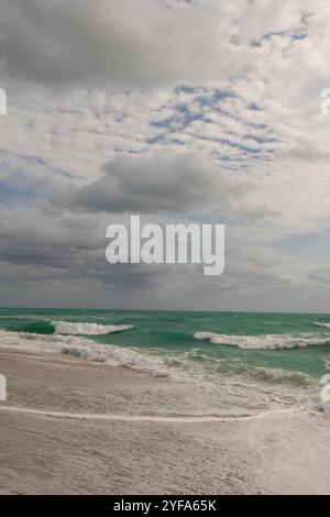 Dolci onde turchesi che raggiungono la spiaggia sabbiosa sotto un cielo nuvoloso Foto Stock