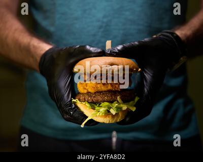 Un uomo sta tagliando un hamburger su un tagliere di legno. L'hamburger è condito con lattuga e cipolle Foto Stock