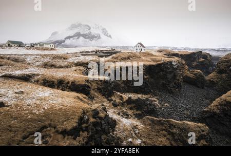 Paesaggio islandese con una piccola e bella casa bianca in inverno sotto la montagna nella penisola di Arnarstapi, Islanda, Europa Foto Stock