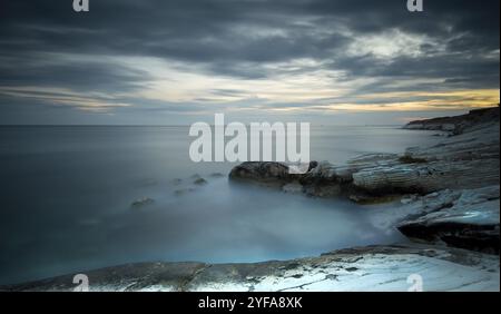 Bel tramonto su una spiaggia rocciosa con acqua in movimento. Fotografie con lunghi tempi di esposizione Foto Stock