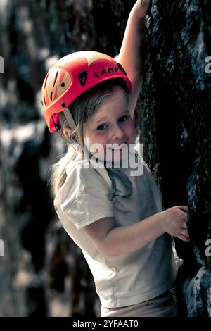 bambina di 5 anni che si arrampica e bouldering con scarpe da arrampicata rosse e nere. Foto Stock