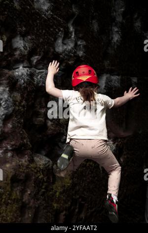 bambina di 5 anni che si arrampica e bouldering con scarpe da arrampicata rosse e nere. Foto Stock