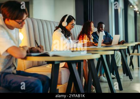 Una vivace scena di biblioteca universitaria con studenti impegnati a studiare, utilizzare computer portatili e libri, mettendo in mostra l'apprendimento collaborativo e la concentrazione. Foto Stock