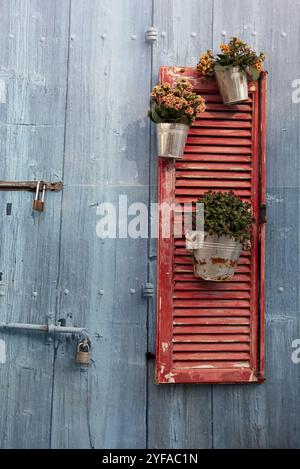 Finestra rossa con telaio in legno con vasi di fiori che decorano una porta blu vintage in legno Foto Stock