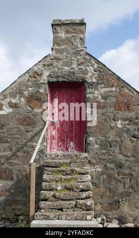 Facciata di un tradizionale cottage scozzese contro il cielo nuvoloso blu. Porta chiusa rossa Foto Stock