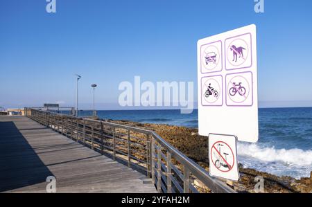 Sentiero pubblico costiero in legno. Segnaletica con icone motore in movimento proibito sul percorso Foto Stock