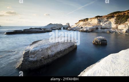 Costa rocciosa con l'oceano ondulato e il suggestivo e bellissimo tramonto nelle grotte marine della zona costiera di Paphos, Cipro, Europa Foto Stock