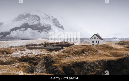 Tipico paesaggio invernale islandese con una piccola e bella casa bianca sotto la montagna nella penisola di Arnarstapi, Islanda, Europ Foto Stock