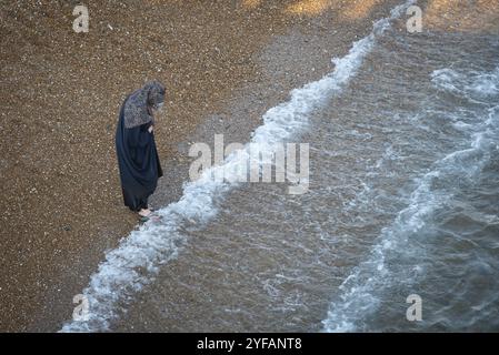 Brighton, Regno Unito, 10 giugno 2023: Donna musulmana araba con tradizionale abito nero che cammina sulla spiaggia, Europa Foto Stock