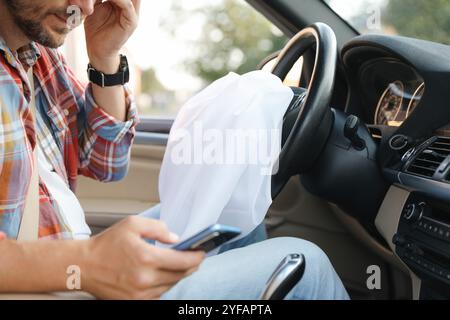 Uomo che usa lo smartphone vicino all'airbag aperto in auto dopo un incidente d'auto, primo piano Foto Stock