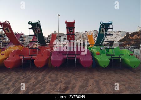 Vivaci pedalò con scivoli di colore rosa, verde e rosso acceso allineati sulla spiaggia Foto Stock