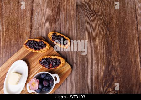 Colazione rustica con marmellata di mirtilli, toast e un piatto di burro, disposti su un tagliere sopra un tavolo di legno scuro dall'alto Foto Stock