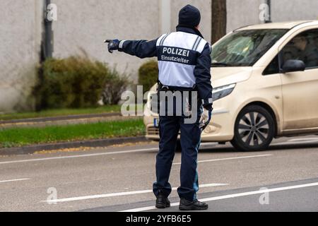 Augusta, Baviera, Germania - 4 novembre 2024: Ufficiale di polizia o ufficiale di polizia del controllo operativo, o capo delle operazioni della polizia bavarese in Svevia di Augusta, incarica CAB di fermarsi, allo sciopero di allerta DELL'UOMO DELL'IG Metall. *** Polizist bzw. Polizeibeamter der Einsatzleitung, bzw. Einsatzleiter der bayrischen Polizei ad Augusta Schwaben, weist taxi zum Anhalten ein, beim IG Metall Warnstreik der MAN. Foto Stock