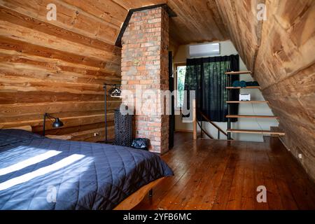 Una camera da letto in legno dal design rustico, camino in mattoni a vista e scalinata in legno, inondata di luce naturale. Foto Stock